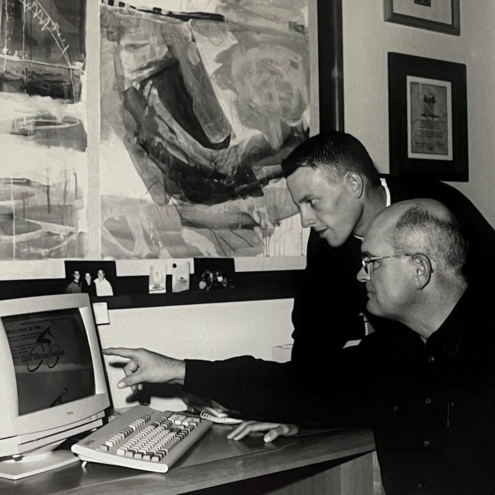 Black and white photo of two men looking at a desktop computer