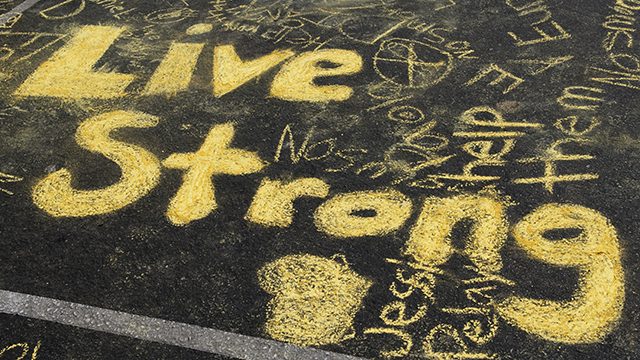 "Live Strong" written in yellow chalk on asphalt ground