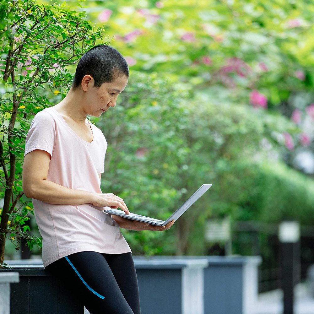 Woman with short hear wearing pink shirt using a laptop computer outside in a garden
