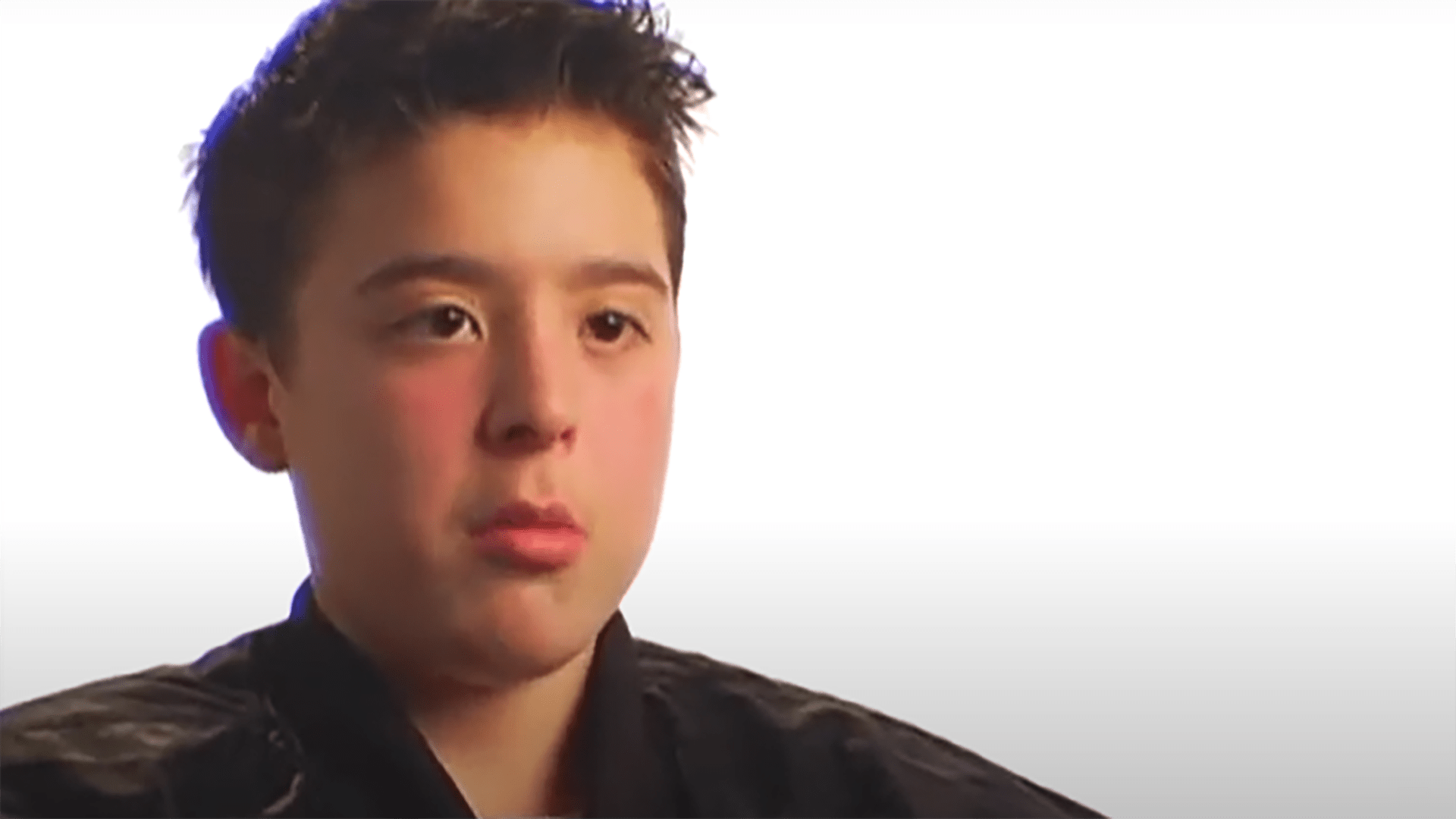 A young boy wearing a black shirt is interviewed against a white background