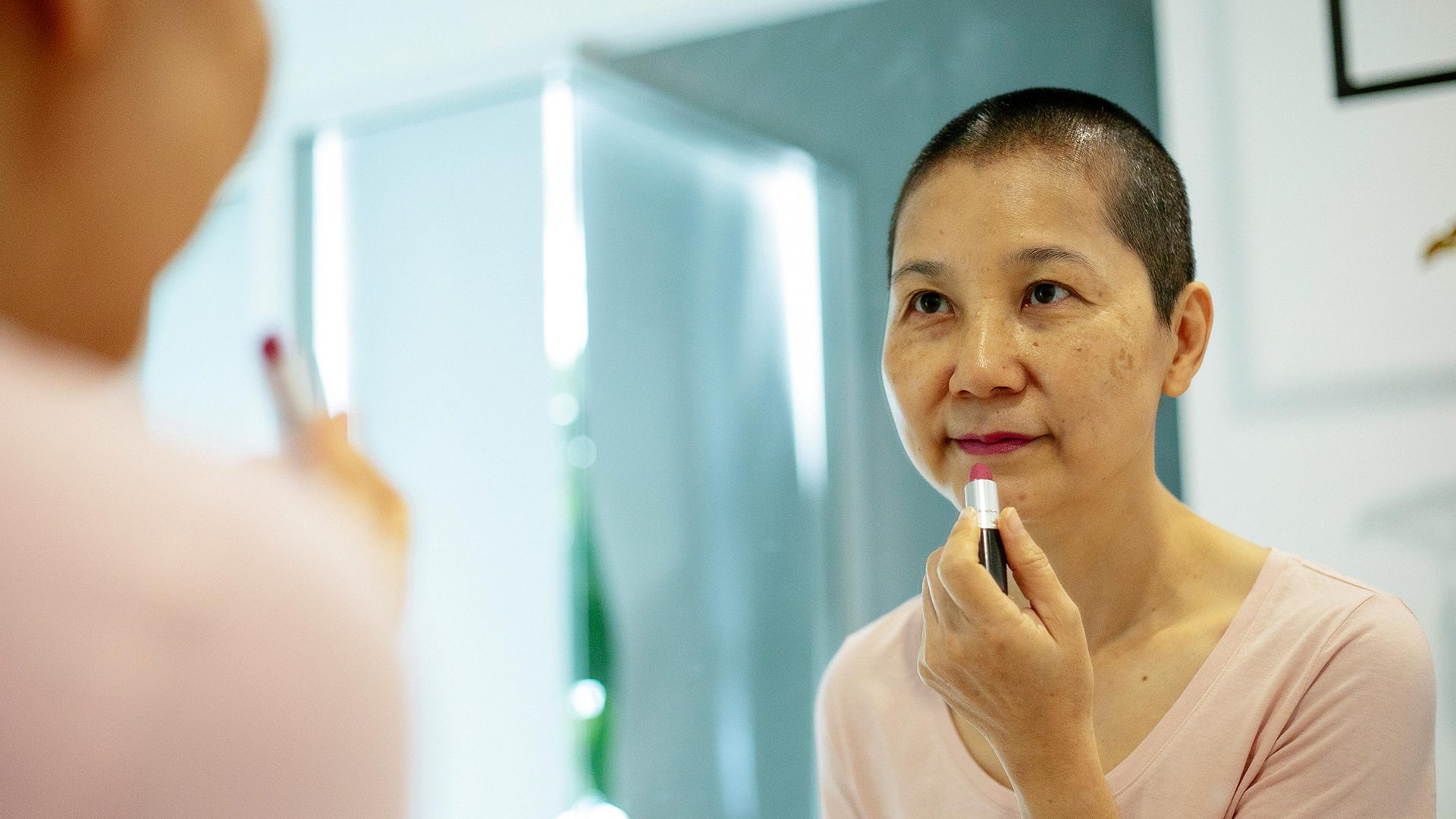 A middle aged woman with cancer applying lipstick in the mirror