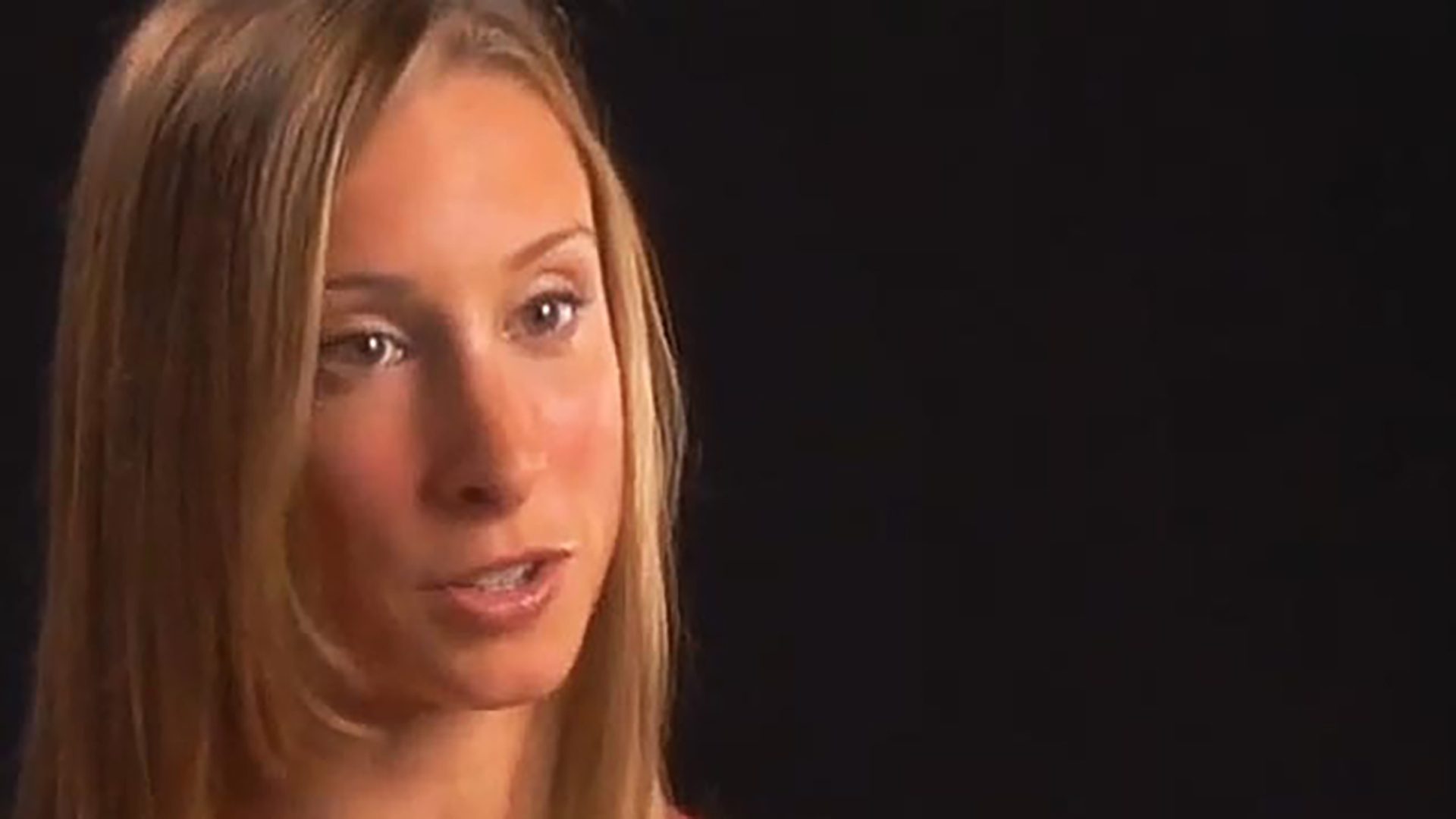 A young blonde woman is interviewed against a black background