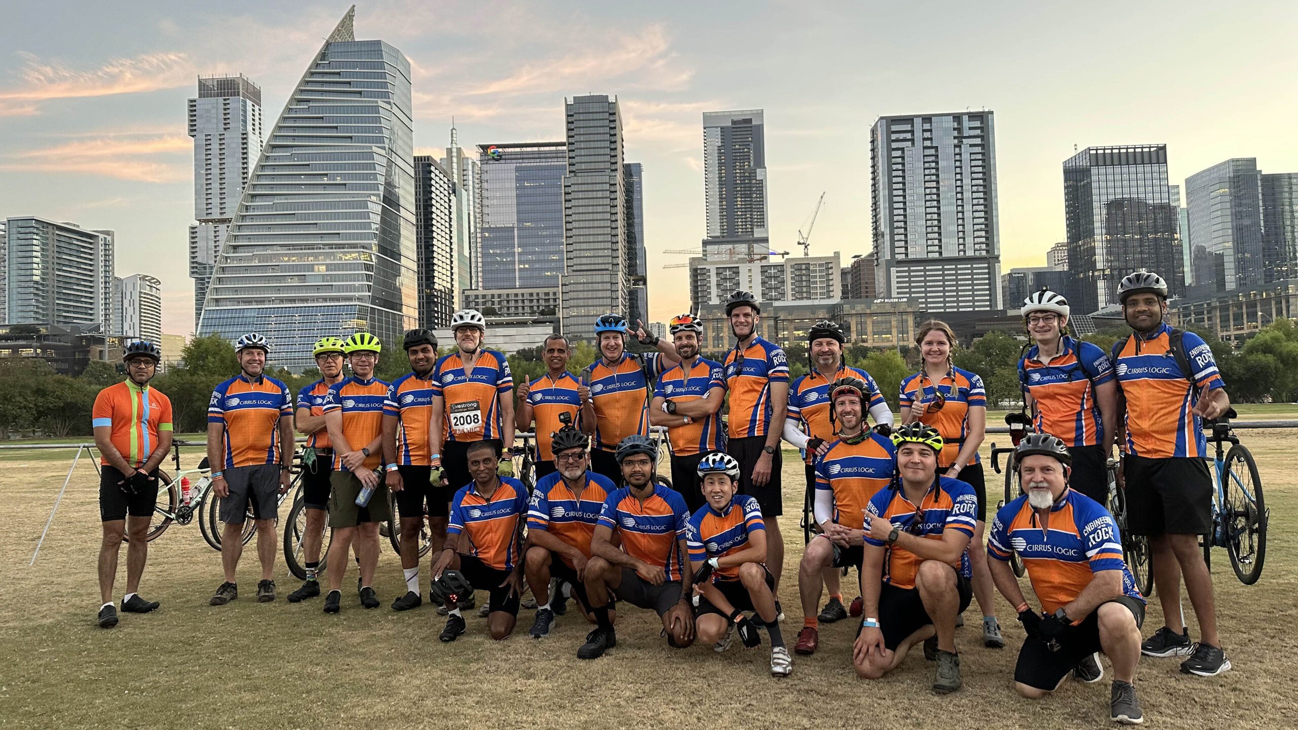 Group of cyclists wearing orange jerseys posing in front of city skyline