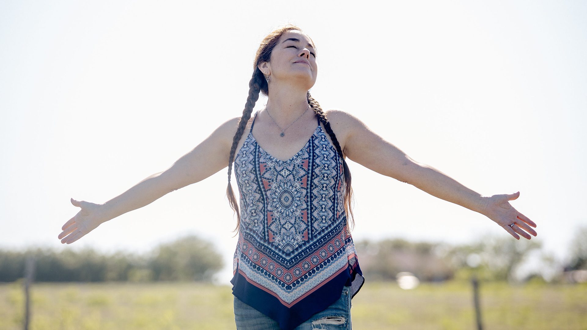 A woman outdoors with her arms outstretched looking toward the sun