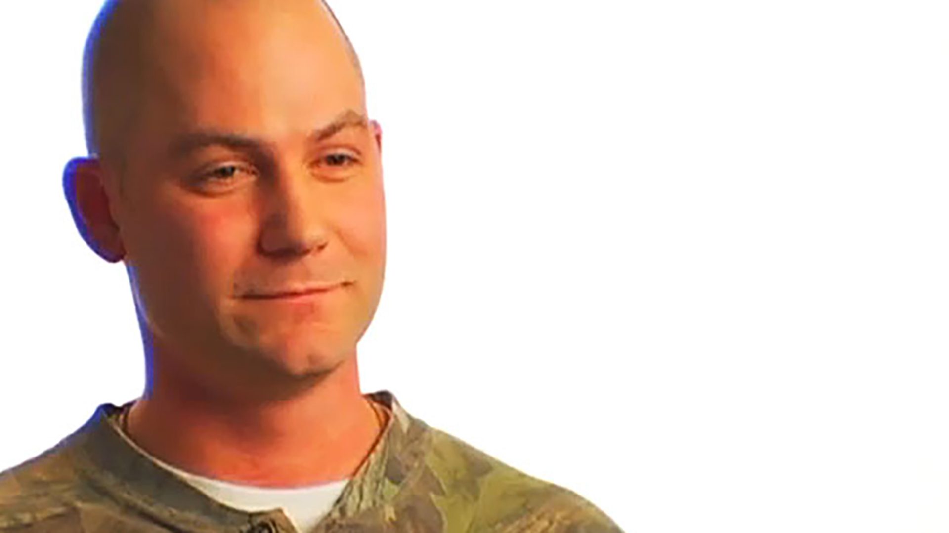 A bald adult man wearing a camo shirt is interviewed against a white background