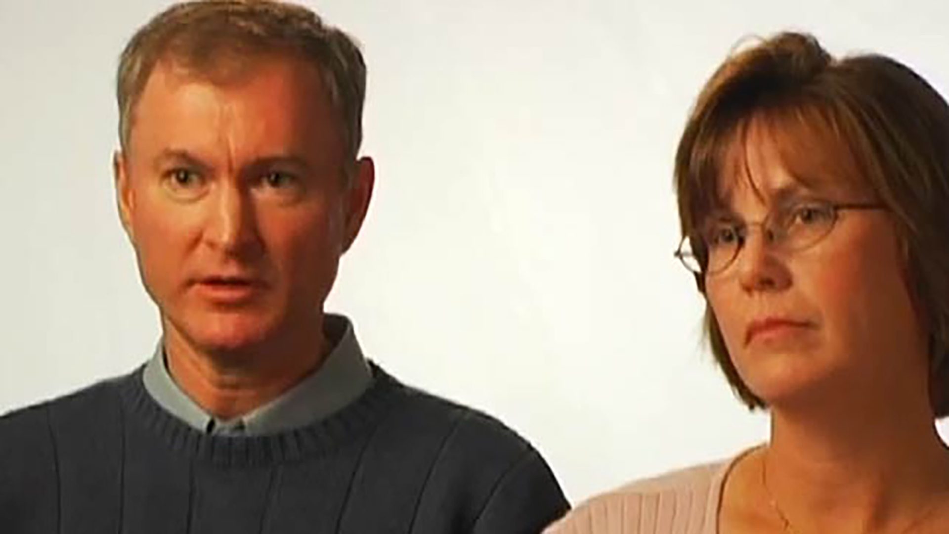 A caucasian man and woman being interviewed against a white background