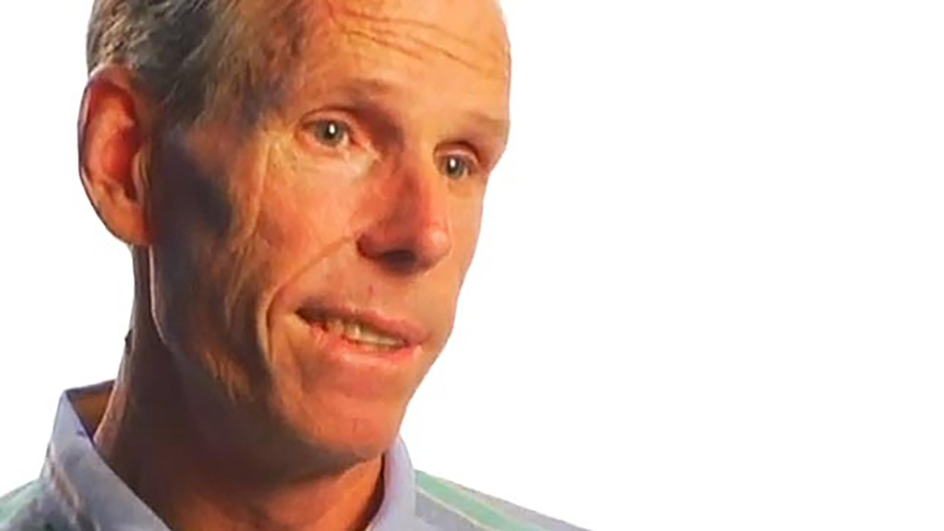 A middle-aged man wearing a pastel collared shirt is interviewed against a white background.