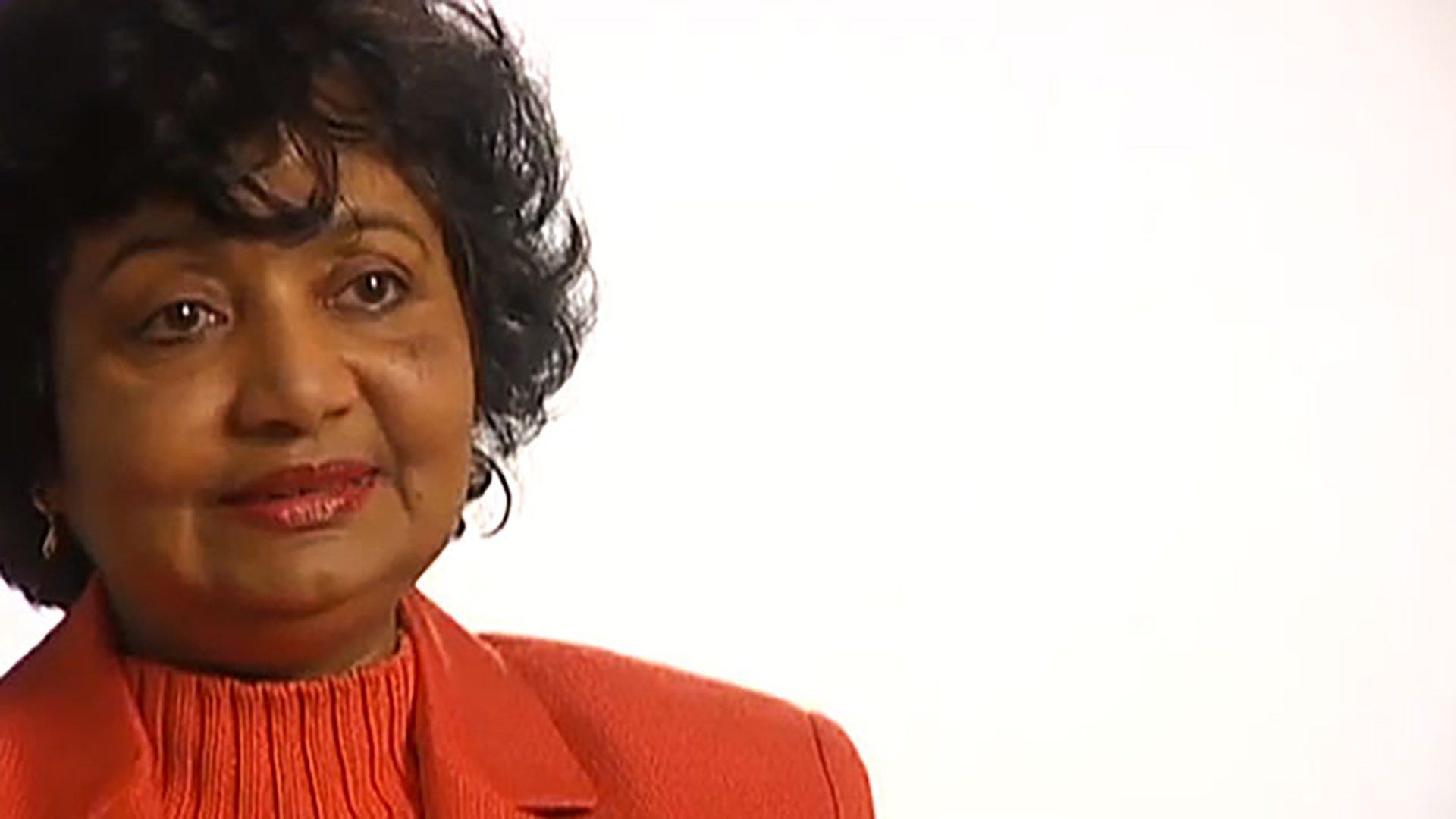 A middle aged woman wearing a red coat is interviewed on a white background