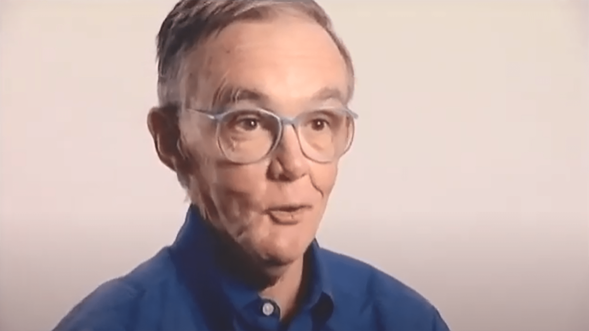 A senior gentleman is interviewed wearing glasses and a blue shirt