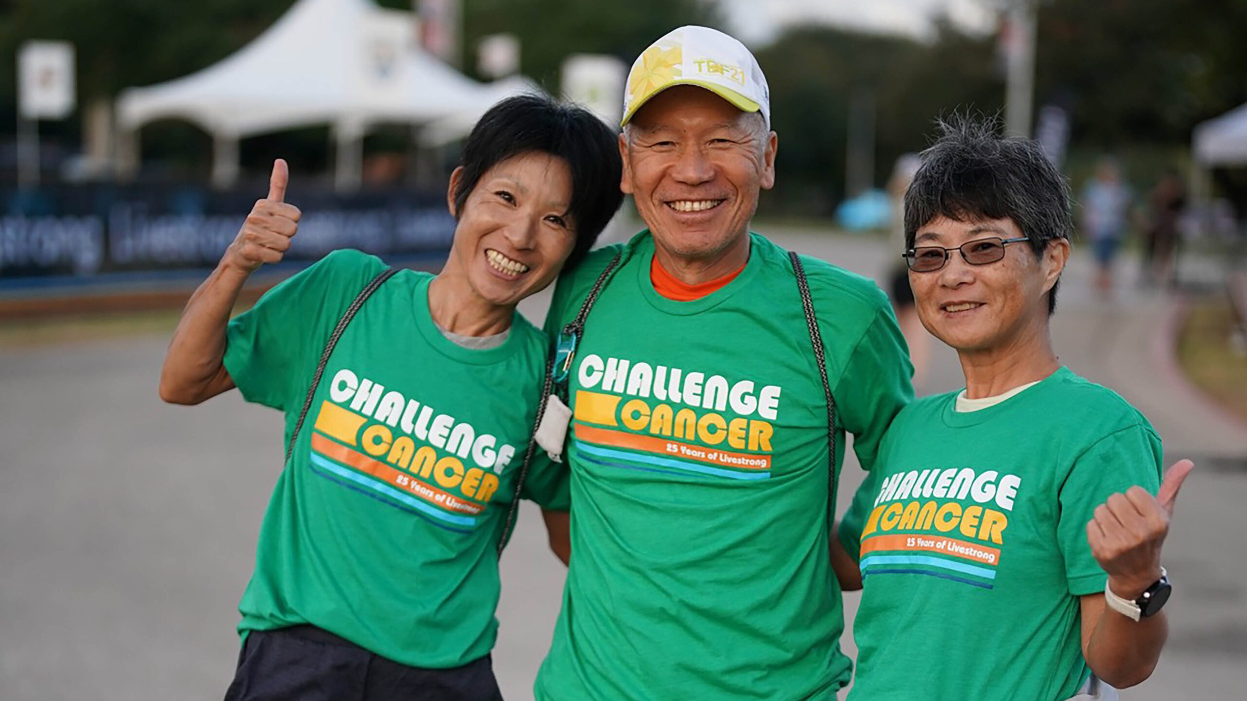 3 smiling adults wearing green "challenge cancer" shirts