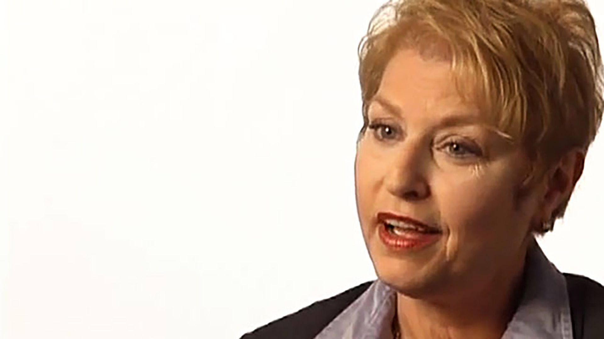 A middle-aged woman with short blonde hair is interviewed against a white background.