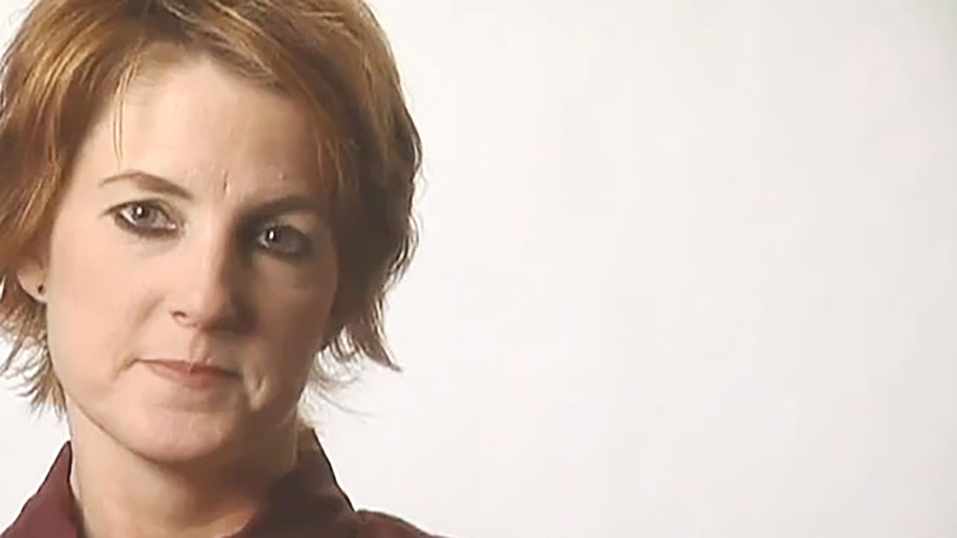A portrait of a woman with short hair wearing eye makeup and a maroon collared shirt