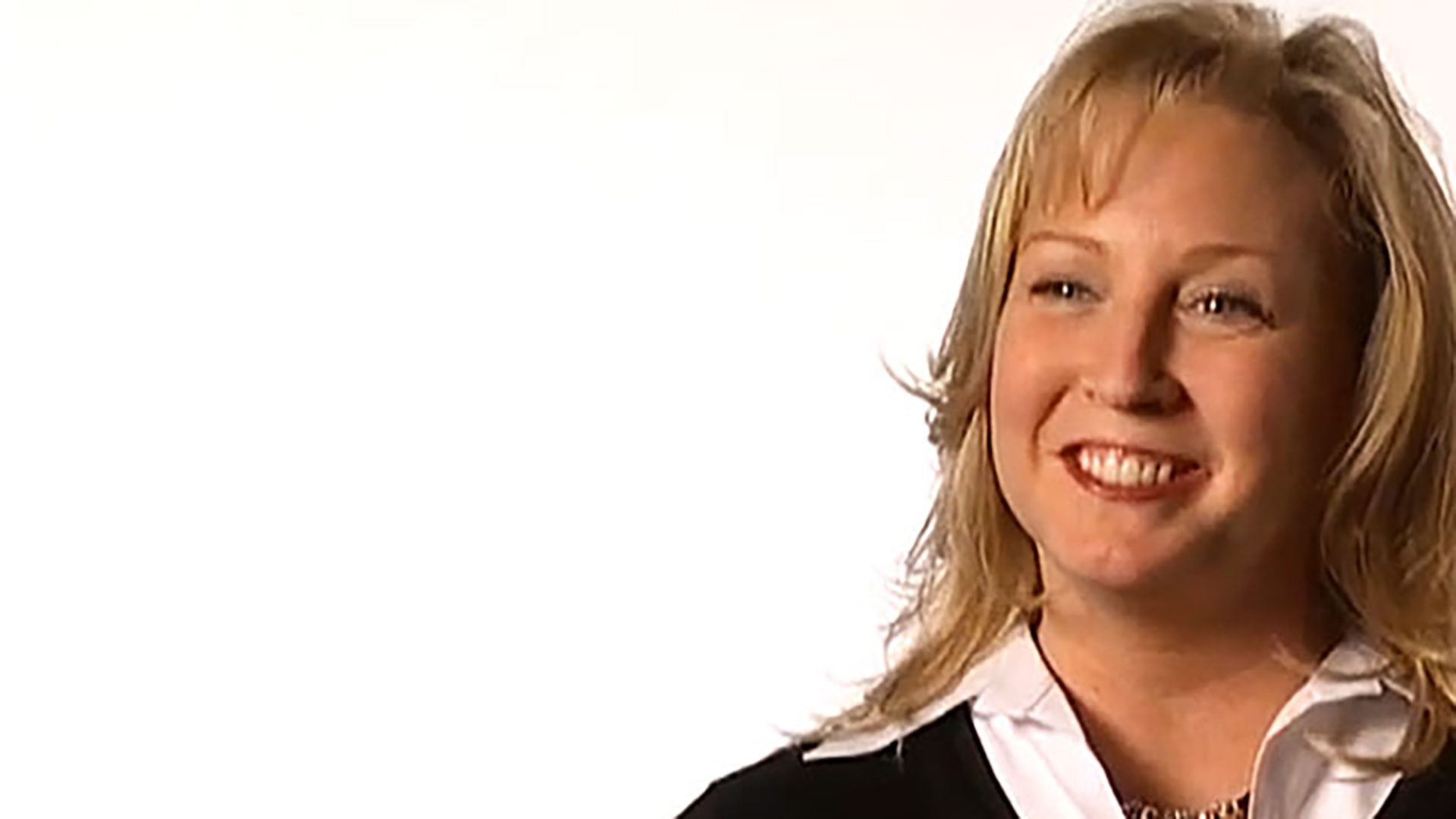 A middle-aged blonde woman wearing professional attire is interviewed against a white background.