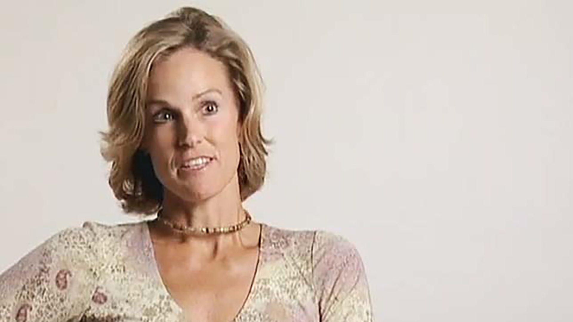 A blonde woman in a patterned shirt being interviewed against a white background