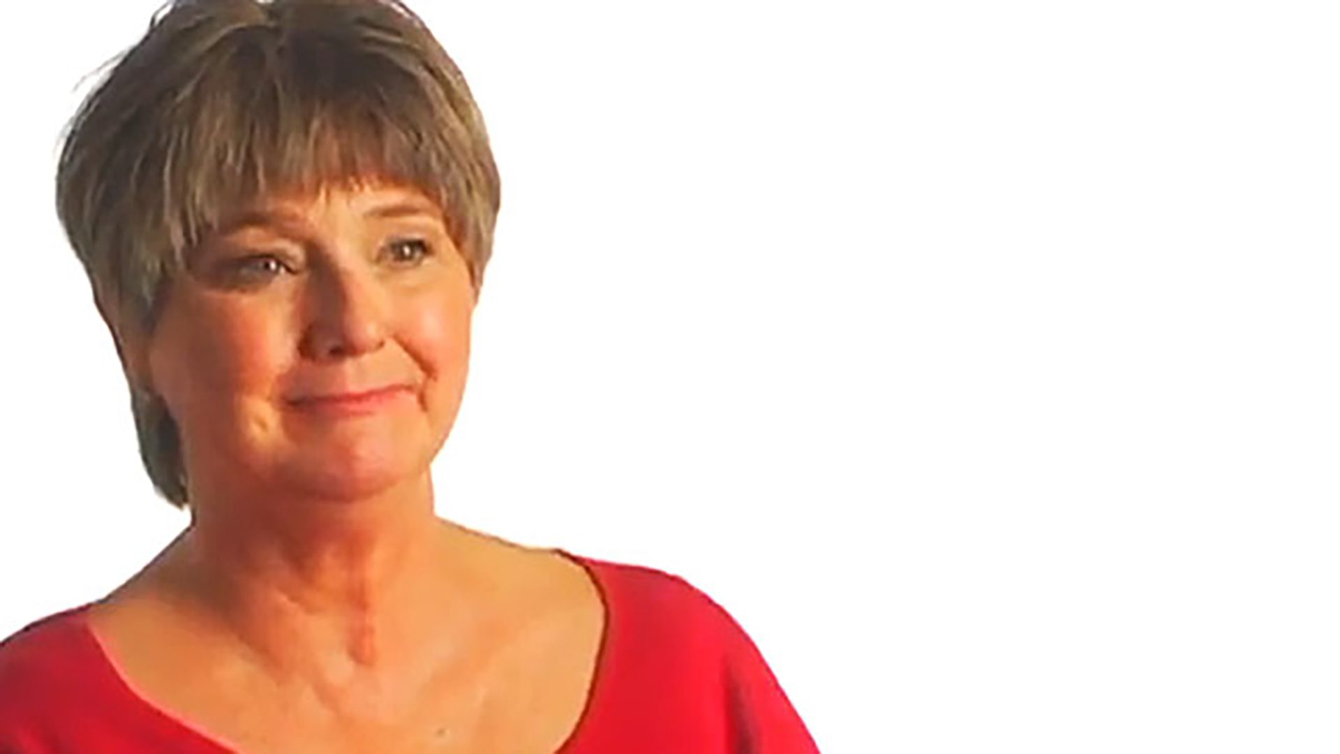A middle-aged woman with short hair wearing a red shirt is interviewed against a white background.