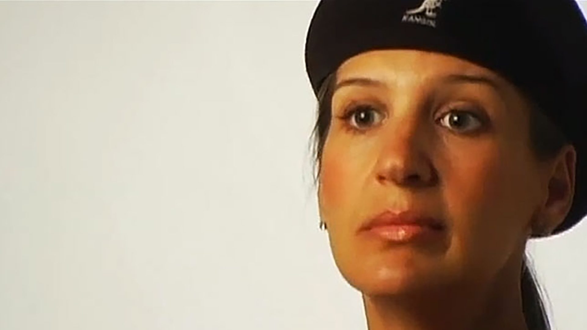 A close-up of a young woman wearing a black beret being interviewed against a white background