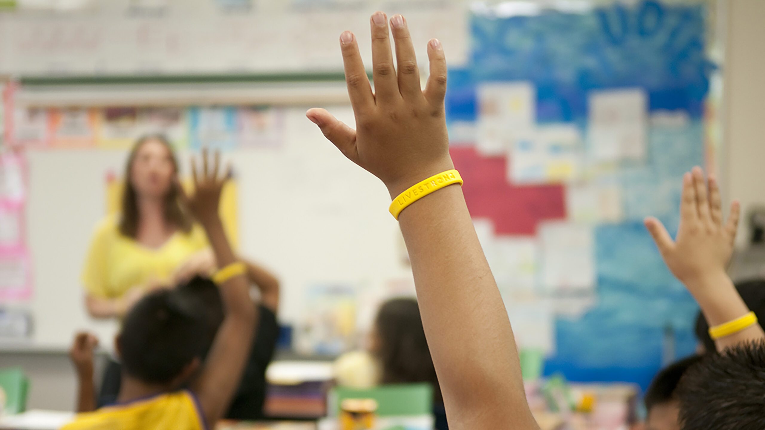 Hand wearing yellow Livestrong wristband raised in a classroom