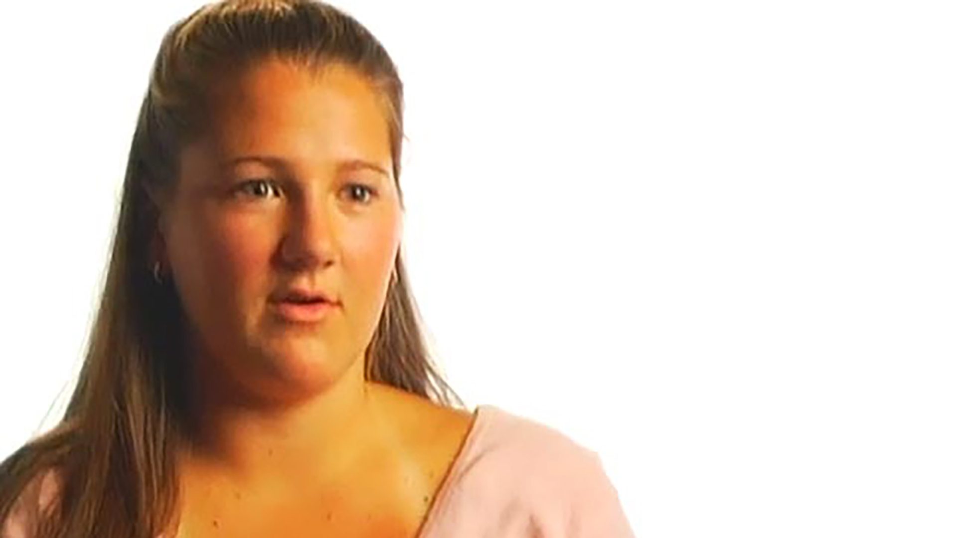 A young adult woman wearing a pink shirt is interviewed against a white background.
