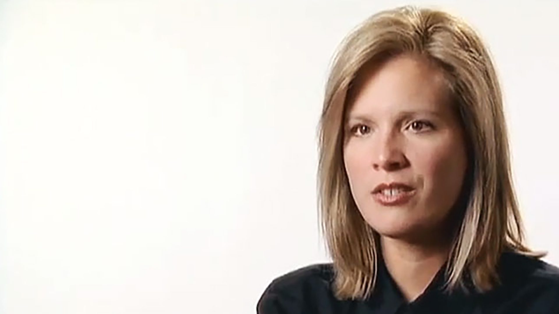 A young blonde woman wearing a black shirt is interviewed against a white background