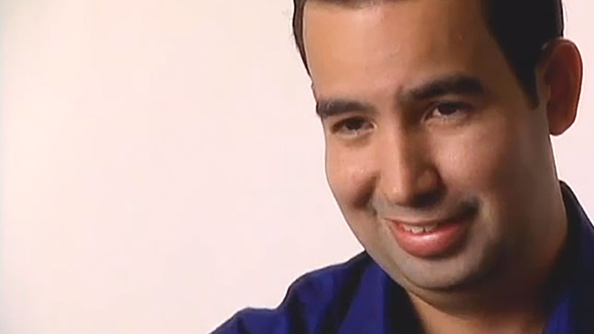A close-up portrait of a smiling man wearing a blue shirt