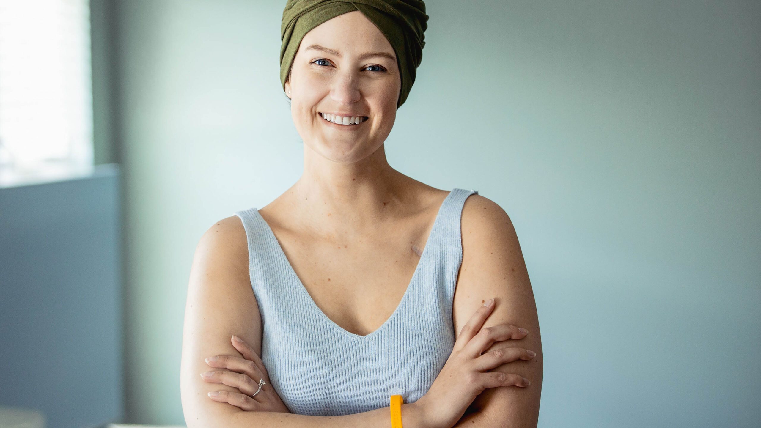 A smiling cancer survivor wearing a green head wrap and Livestrong wristband
