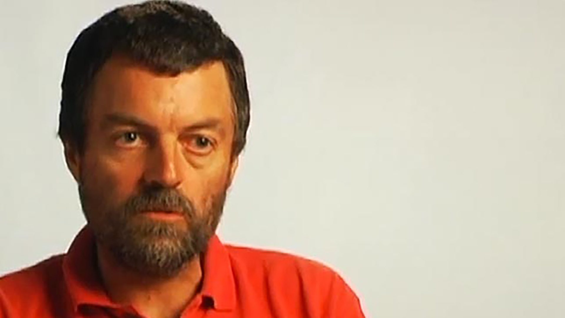 An adult man being interviewed wearing a red polo shirt