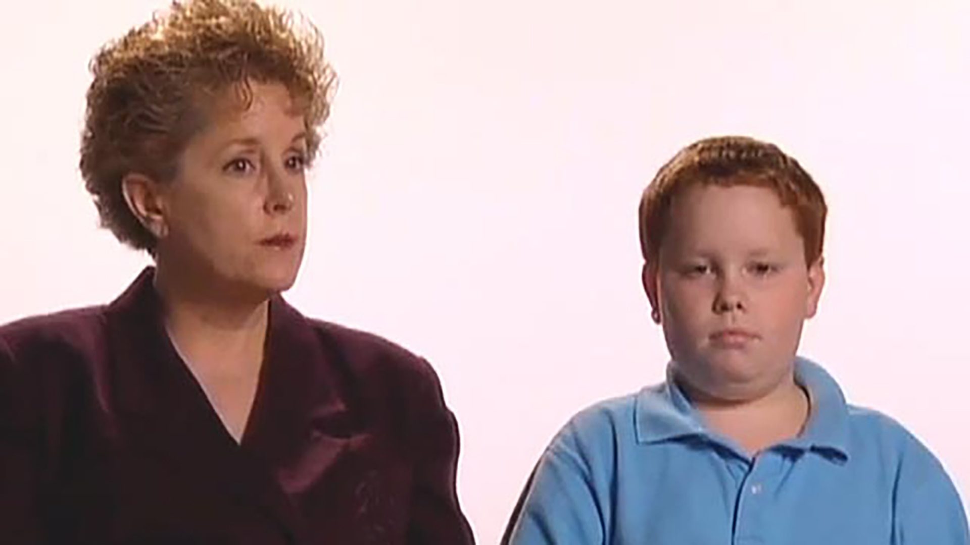 A woman in a burgundy suit jacket and a young boy in a light blue polo shirt are interviewed against a white background.