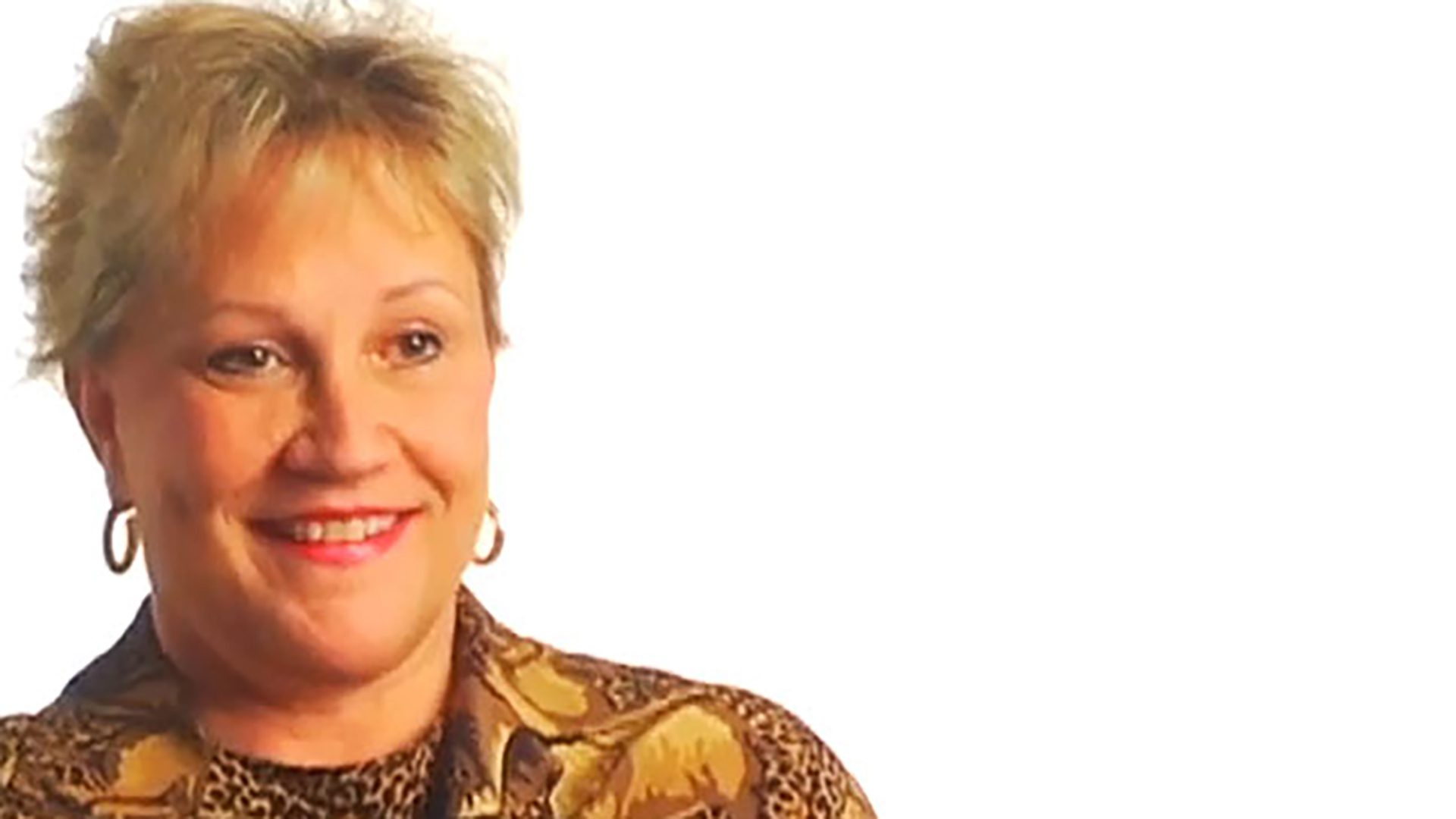 A middle-aged woman with short blonde hair wears an animal-print shirt and is interviewed against a white background.