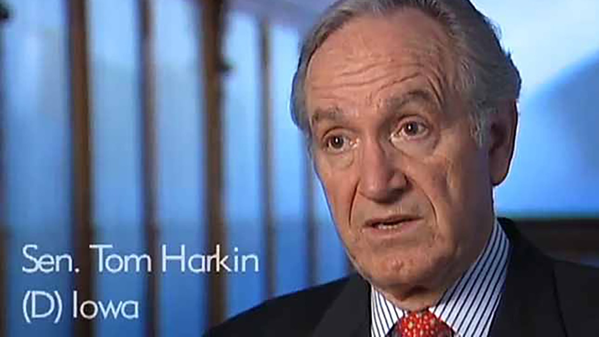 A professional senior man is interviewed against a blue background. Text on the image says Sen. Tom Harkin (D) Iowa.