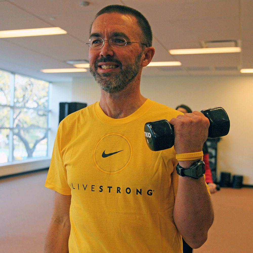 Man wearing yellow Livestrong shirt lifting dumbbell