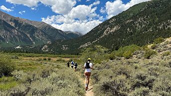 Runners on a trail in Leadville, CO with an expansive view of mountains in the distance.
