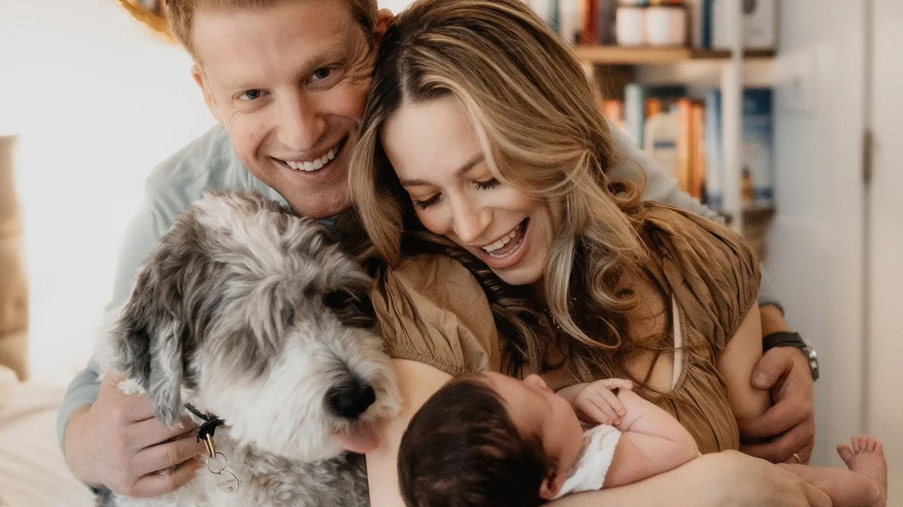 A father and mother hold their newborn baby and gray dog