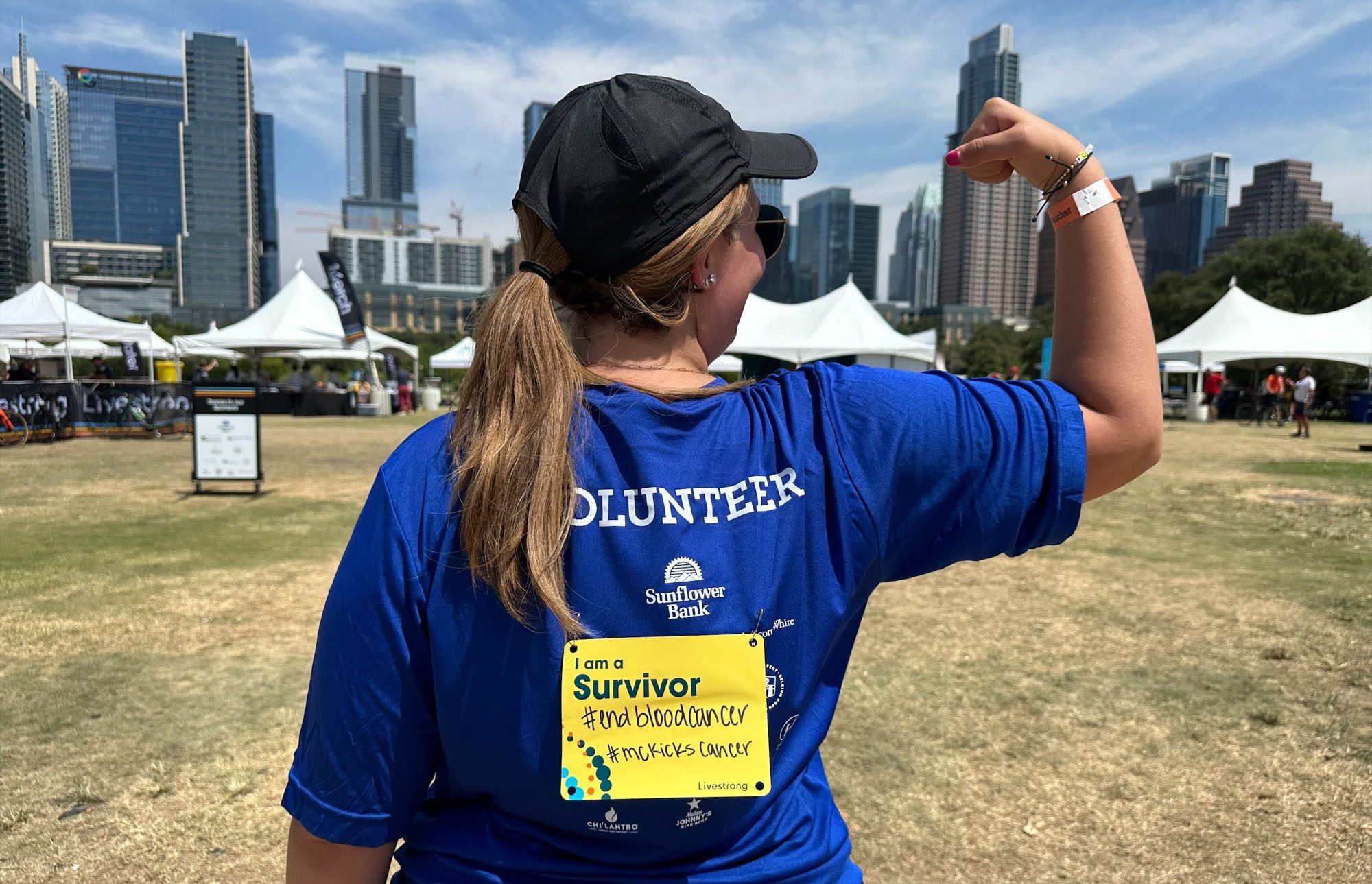 A young woman flexes her arm and displays a cancer survivor card on her back