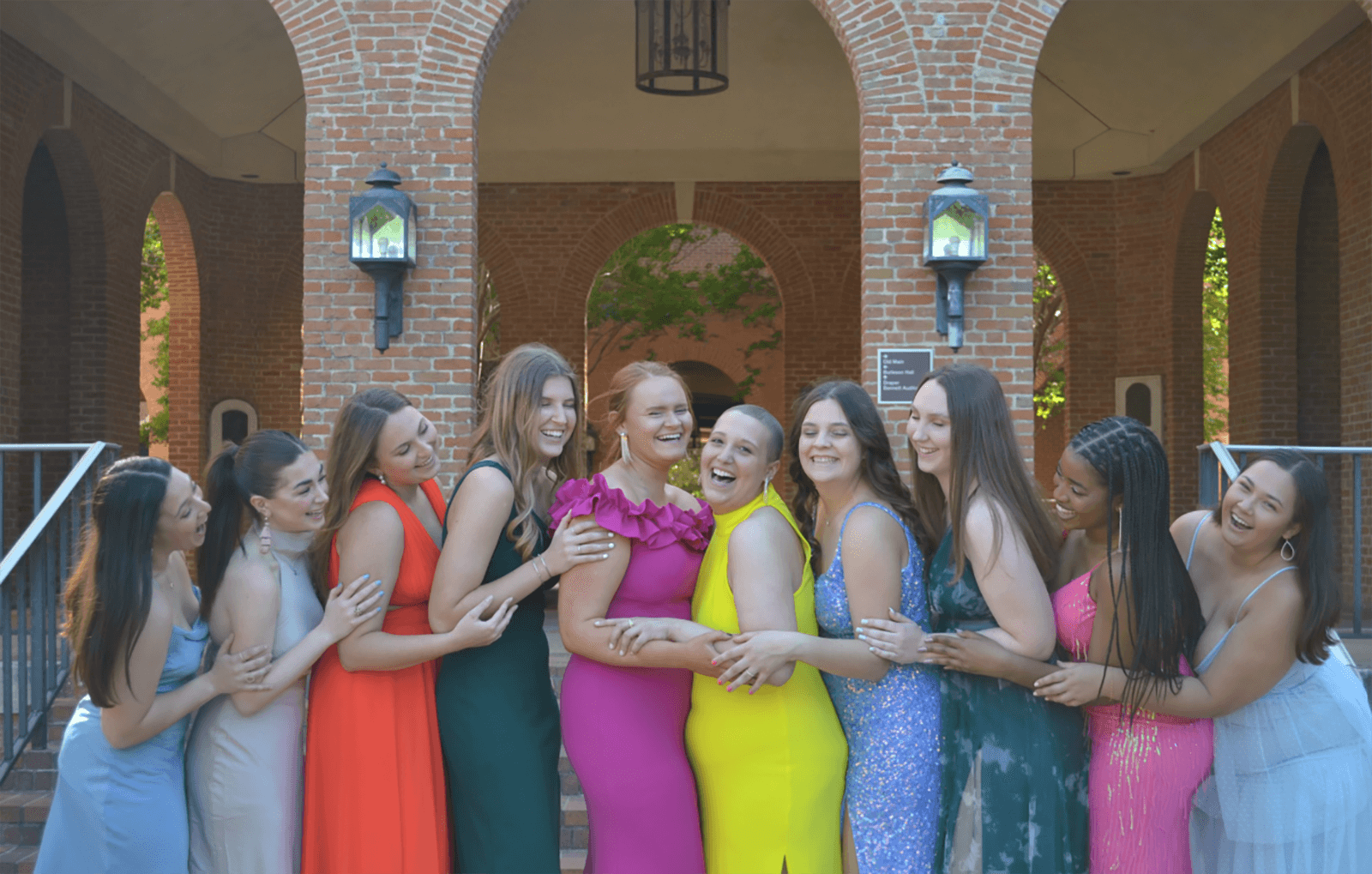 Young women wearing formal dresses embrace in a line