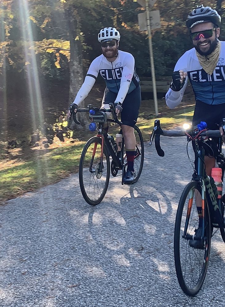 Two smiling men in matching jerseys riding bikes