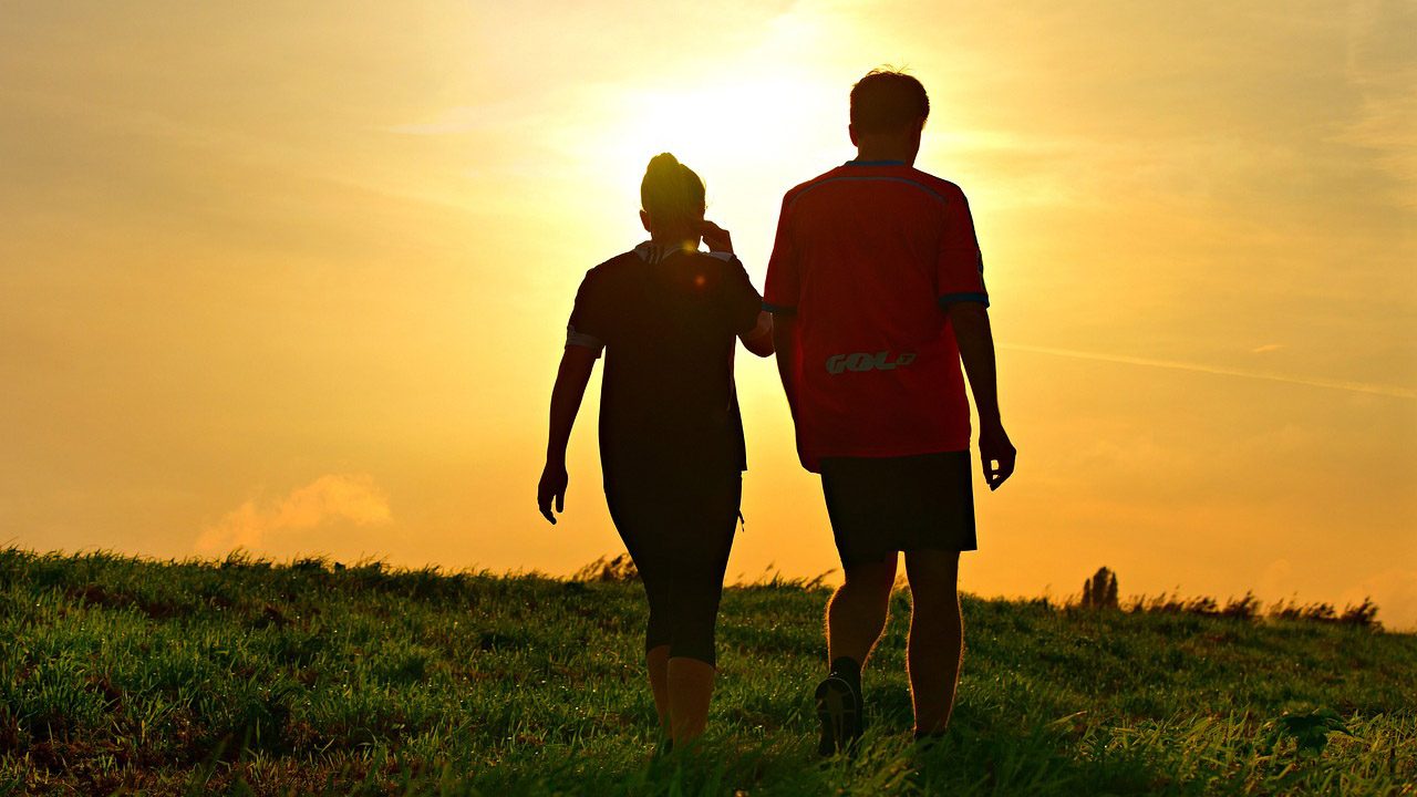 A silhouetted woman and man walking outdoors during a sunset