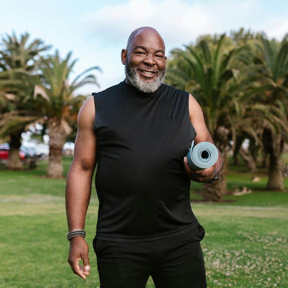 A middle-aged man in exercise clothing holding a yoga mat