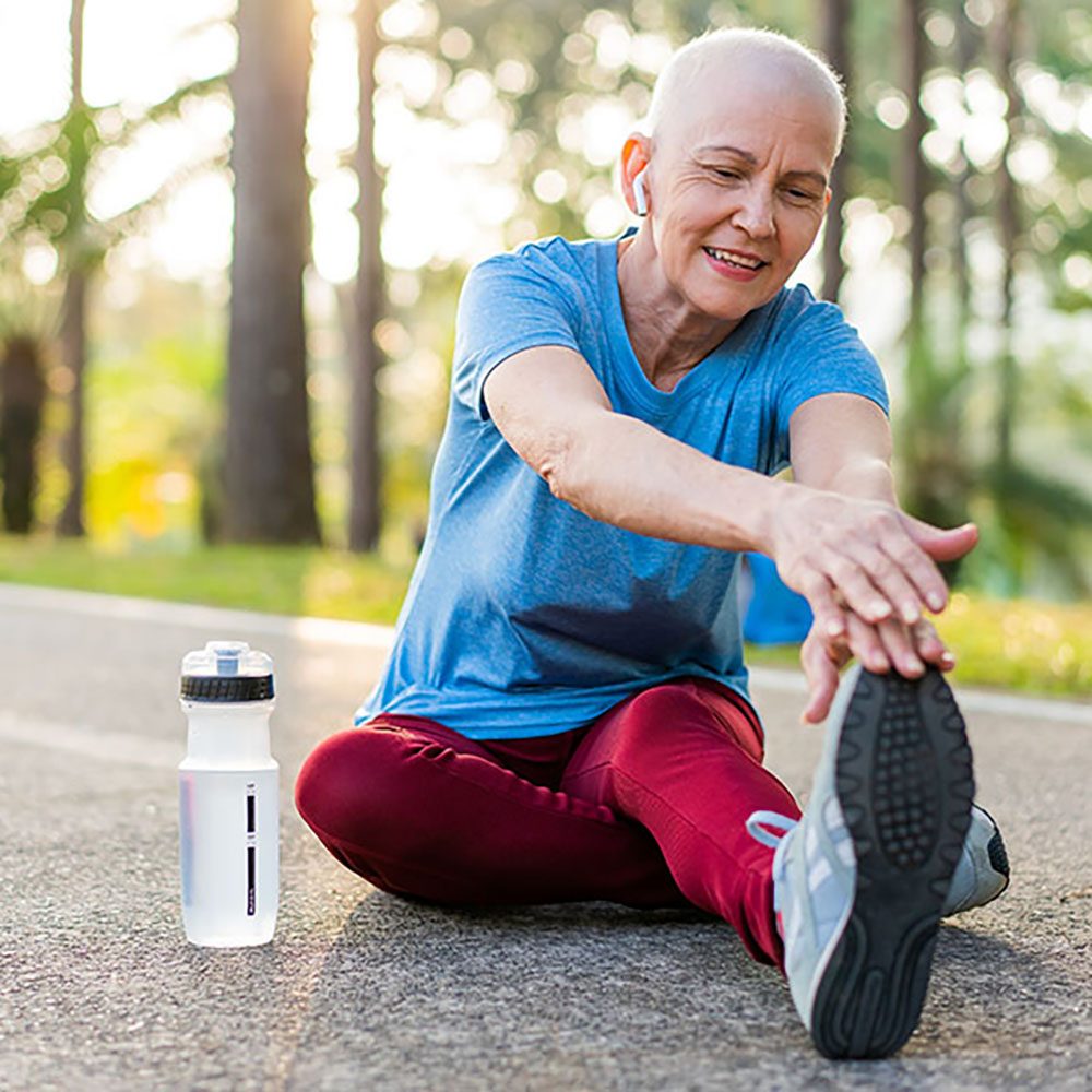 A senior woman cancer survivor stretches her leg outdoors