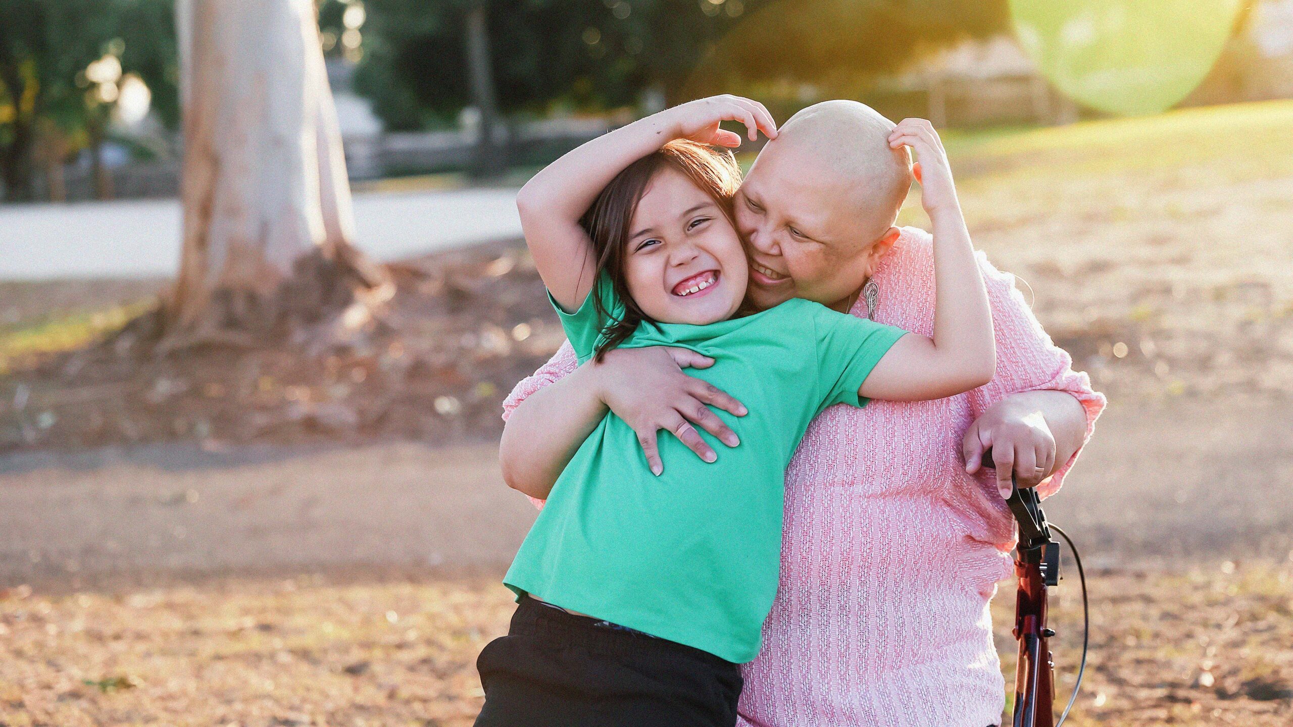 A cancer patient and her young child hug in a park