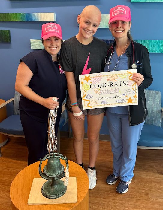 A teen cancer survivor stands with a nurse and doctor holding a congrats certificate