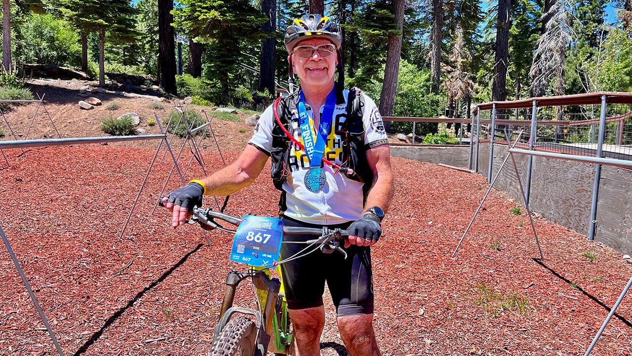 A senior male cyclist smiles wearing a medal