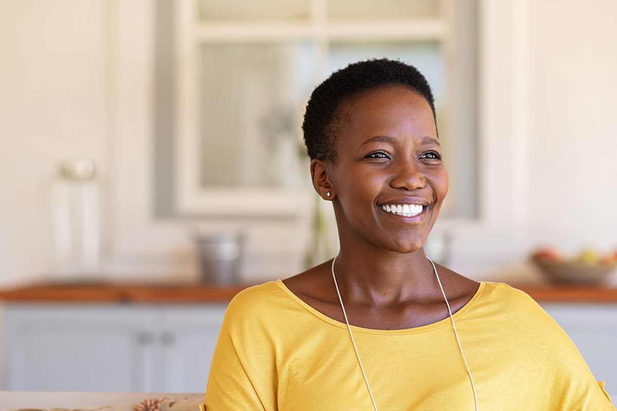 A mature woman in a yellow shirt smiling and looking into the distance