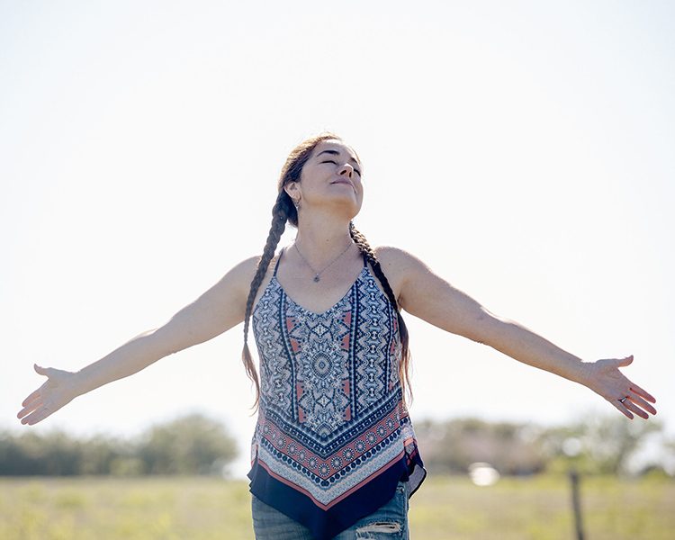 A woman outdoors raising her arms in the sun