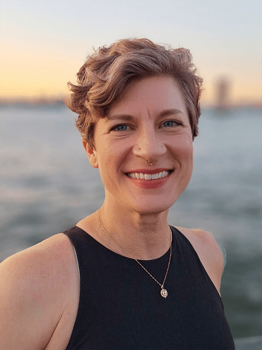 A portrait of an adult woman in front of a body of water at sunset