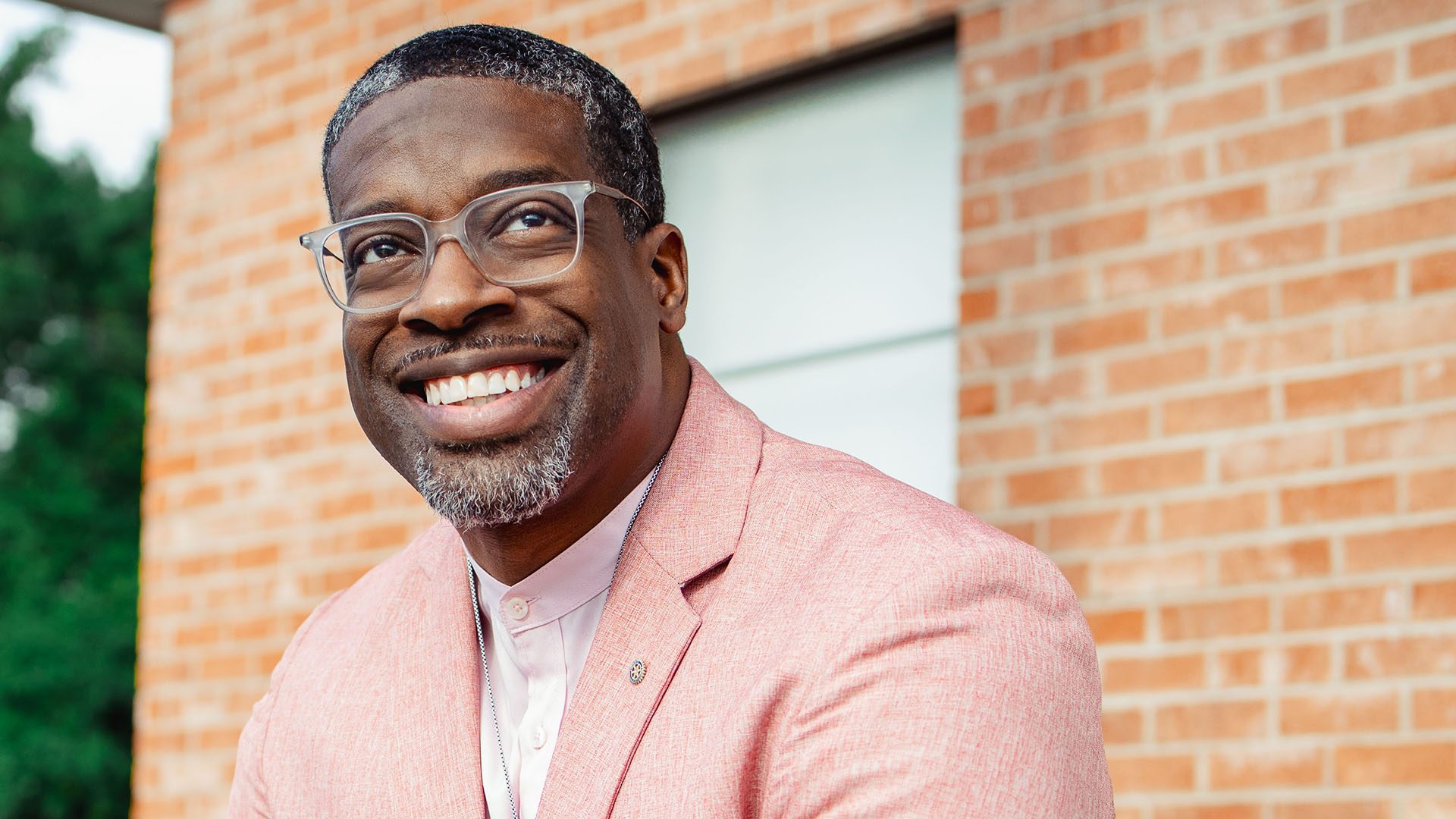 A mature man smiling next to a brick wall