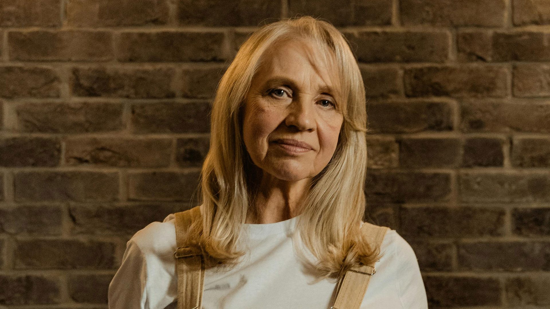 Mature Woman in White Long Sleeve Shirt Standing Beside a Brick Wall