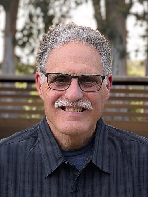 A headshot of a mature adult man wearing glasses