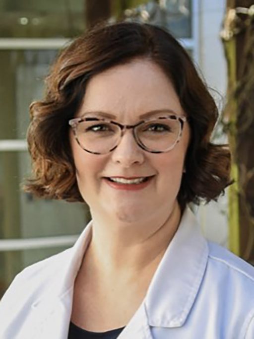 A headshot of an adult woman wearing glasses and a white coat