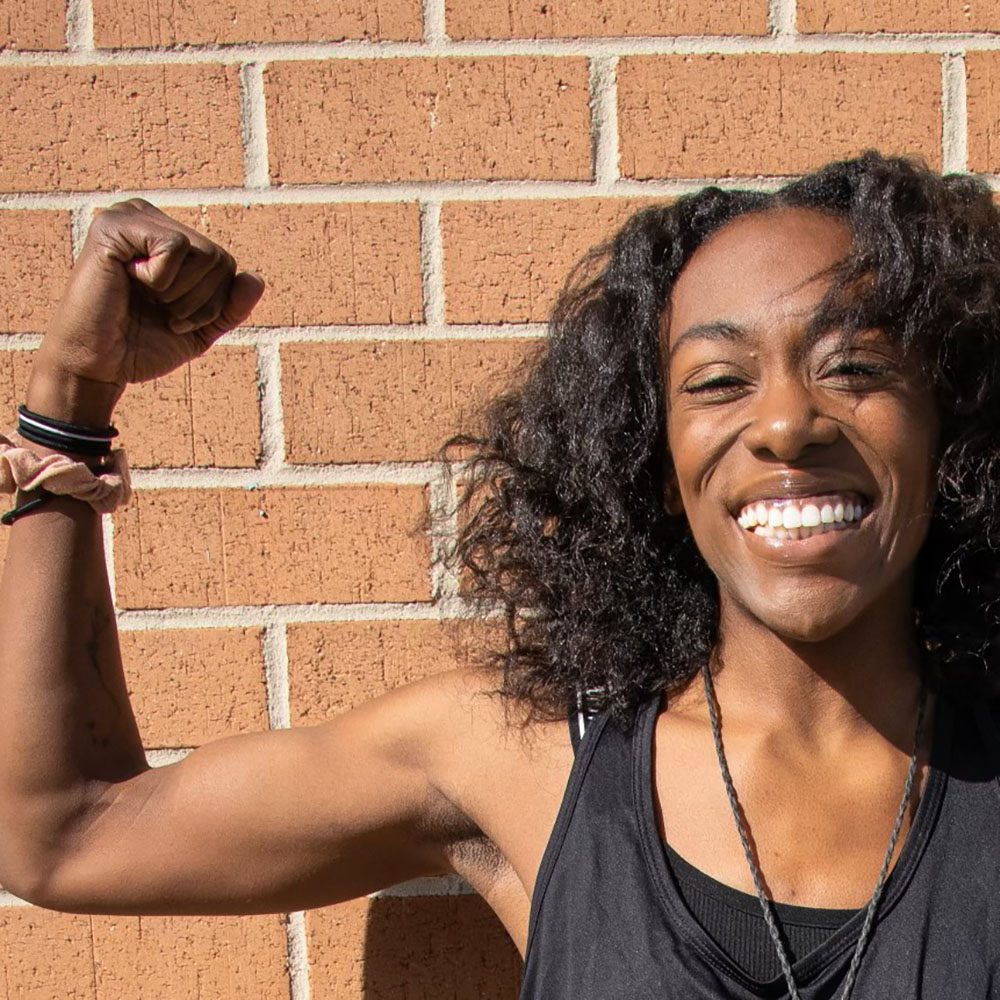 An adult woman flexing her arm against a brick wall