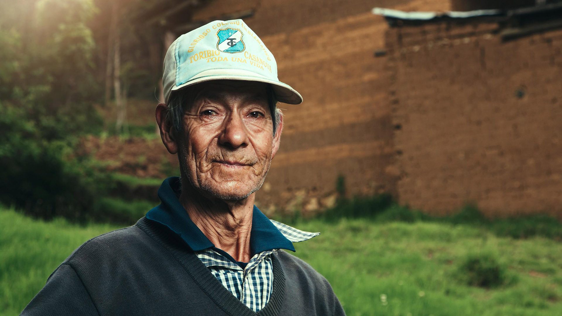Portrait of a senior gentleman wearing a hat with a background of a brick wall and grass